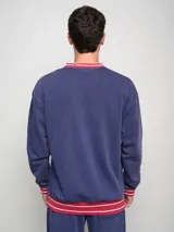 Buzo azul marino de felpa con efecto lavado, cuello en V y puños en color rojo con rayas blancas. Presenta el escudo del Club Nacional de Football y el logo de Umbro bordados en el pecho.