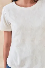 Remera blanca de manga corta con cuello redondo y bordados florales monocromáticos en relieve.