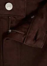 Pantalón de jean acampanado color marrón oscuro, con tiro alto, cinco bolsillos y cierre frontal con cremallera y botón.