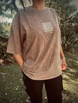 Remera oversize color marrón con estampa en la espalda de un sol naciente sobre el mar.