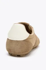 Zapatillas deportivas color beige con detalles en gamuza, estilo running, con suela dentada y ajuste con cordones.