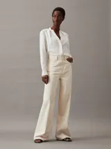 Blusa blanca de poliéster reciclado con escote en V, manga larga y detalle de pliegues en los hombros.