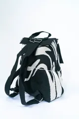 Mochila de tejido con estampado abstracto en blanco y negro, con solapa superior negra y asa de mano.
