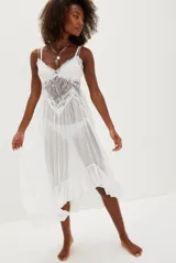 Vestido blanco de encaje con transparencias, breteles finos y volados en el ruedo.