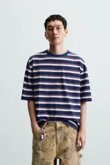 Camiseta de hombre a rayas horizontales azul marino, blancas y rojas, de corte holgado, cuello redondo y mangas cortas.