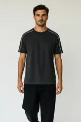 Remera de algodón color gris oscuro con efecto lavado, corte holgado y cuello redondo. Presenta un ribete blanco fino que recorre la costura del hombro y el borde de la manga.