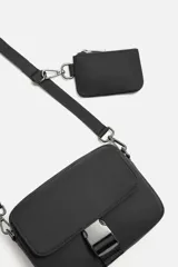 Bandolera negra de tela técnica con correa ajustable y extraíble. Tiene un compartimento principal con cierre de cremallera, un bolsillo interior con cremallera, un bolsillo frontal con solapa y hebilla de liberación rápida, y un monedero removible.