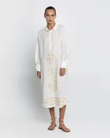 Vestido largo tipo camisero color blanco, con bordados dorados, cuello con botones y mangas largas. Incluye enagua.