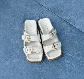 Sandalias bajas color crema con dos tiras anchas con hebillas doradas y suela plana.