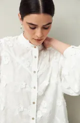 Camisa blanca con bordado floral en contraste, cuello mao, abotonadura frontal y mangas largas con frunces en los hombros.