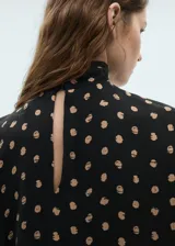 Blusa negra con estampado de lunares color beige, de manga corta y cuello alto con detalle drapeado.