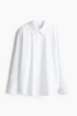 Camisa blanca oversized de popelina de algodón, con cuello clásico, botones frontales, hombros caídos, mangas largas con puños abotonados, canesú con pliegue en la espalda y bajo redondeado.