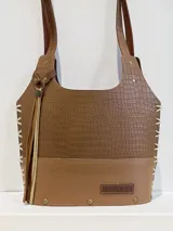 Cartera matera de cuero color marrón con textura tipo cocodrilo en la parte superior y cuero liso en la parte inferior. Tiene dos asas de hombro, cierre superior abierto, colgante de cuero con flecos y base rígida con cuatro remaches metálicos.