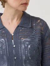 Sweater color crudo tejido a crochet con diseño de cuadrados y círculos, cuello camisero, mangas largas y cierre frontal con botones.