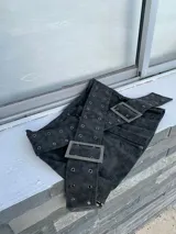 Minifalda negra de gamuza sintética con dos cinturones anchos con hebillas metálicas y ojales.