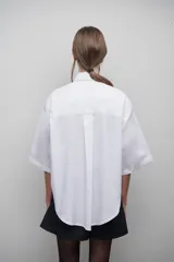 Camisa blanca de popelina 100% algodón, de diseño oversize y corte unisex. Presenta cuello clásico, manga amplia, bolsillo frontal y canesú con pliegue central en la espalda.