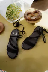 Sandalias bajas de cuero color marrón, con tiras finas para atar alrededor del tobillo.