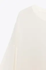 Top amplio color blanco, de cuello redondo y manga corta por debajo del codo. Bajo con aberturas laterales.