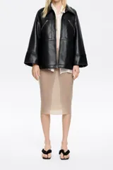 Chaqueta negra de cuero sintético con cuello camisero, cierre frontal con cremallera, bolsillos con cremallera en el pecho y mangas largas con cremalleras en los puños.