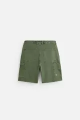 Bermuda color verde militar, de corte relaxed fit, con bolsillos frontales y traseros tipo plaqué, detalle de tira y bolsillo multifunción en la pierna, y bajo irregular.