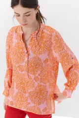 Camisa de mangas largas con estampado floral en tonos naranja sobre fondo rosa. Tiene cuello mao y cierre frontal con botones.