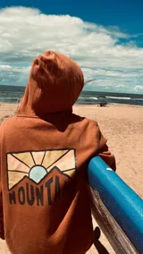 Buzo hoodie color ladrillo con estampado en la espalda de montañas y sol.
