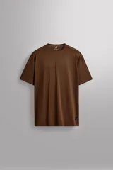 Camiseta deportiva marrón confeccionada en tejido técnico ligero y elástico con estructura perforada. Cuello redondo, manga corta y bajo asimétrico con aberturas laterales. Detalle de logo estampado.