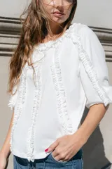 Blusa blanca de algodón con mangas 3/4 y escote redondo con volados en el frente, mangas y escote.