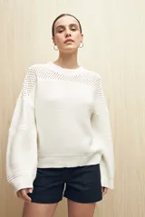 Sweater de punto color salmón con cuello redondo y mangas anchas. Presenta un diseño calado en la parte superior y tejido tramado horizontal en el resto del cuerpo.