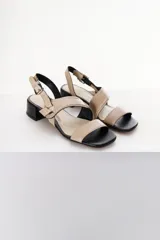 Sandalia de mujer color beige claro con taco bajo y grueso de color negro. Presenta tiras cruzadas en el empeine con un detalle de argolla metálica y tira de ajuste con hebilla en el talón.
