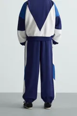 Pantalón deportivo azul marino con paneles laterales blancos y detalles en azul eléctrico. Corte relaxed fit, cintura elástica ajustable con cordón, bolsillos frontales ocultos y puños elásticos.