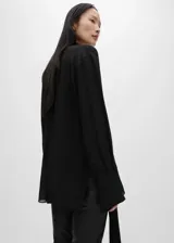 Camisa negra de tejido fluido semitransparente con lazo en el cuello, mangas largas con puños abotonados, diseño recto, cuello camisero, bajo con aberturas laterales y cierre delantero con botones.