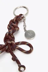 Accesorio charm para bolso con cuerda anudada en tonos borgoña, azul y beige, con abalorios metálicos plateados.
