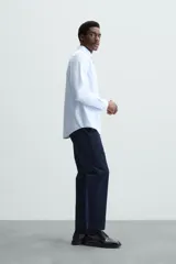 Camisa celeste a rayas verticales blancas, de corte recto, con cuello italiano abierto, mangas largas con puños abotonados y cierre frontal con botones.
