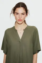 Vestido túnica a la rodilla en tejido liviano de viscosa color verde oliva con cuello mao y abertura en V. Modelo de corte holgado con hombros levemente caídos, mangas cortas y bajo recto con tajos laterales.