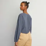 Blusa azul de algodón con textura arrugada, escote en V con lazos y mangas largas abullonadas.