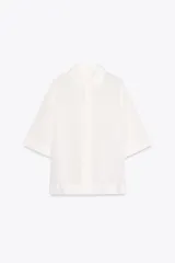 Camisa blanca de corte holgado, con cuello solapa, manga corta y cierre frontal con botones.