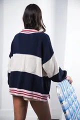 Cardigan tejido a rayas horizontales rojas y crema, con cuello redondo, cierre frontal con botones marrones y mangas largas abullonadas. Presenta ribetes a rayas en cuello, puños y ruedo. Tiene bordado el logo de la marca en el pecho.