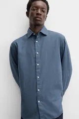 Camisa de vestir azul petróleo, corte regular, confeccionada en mezcla de algodón. Cuenta con cuello solapa, mangas largas con puños abotonados y cierre frontal con botones.