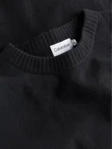 Sweater negro de lana y acrílico con cuello redondo, puños y bajo de canalé. Tiene una insignia con el logo de Calvin Klein en la manga.