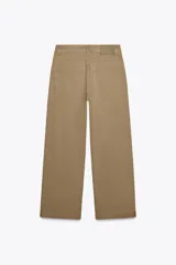 Pantalón cropped color beige de tiro alto y corte recto, confeccionado en algodón. Cuenta con bolsillos delanteros y traseros, trabillas en la cintura y cierre frontal con cremallera y botón.