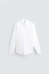 Camisa blanca de algodón, corte regular fit, con cuello solapa, manga larga con puños abotonados y cierre frontal con botones.