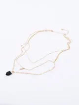 Collar dorado de tres cadenas finas de diferentes largos. La cadena más corta es de eslabones pequeños, la del medio tiene un dije circular y la más larga tiene un dije de piedra facetada negra.