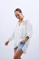 Camisa color crudo con bordado de lentejuelas doradas en el frente, de corte holgado y mangas largas con lazo en los puños.