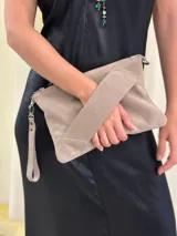 Sobre/cartera de gamuza color marrón oscuro, con diseño de solapa diagonal. Incluye una correa larga para usar al hombro o como bandolera, y una correa corta para la muñeca, ambas desmontables.