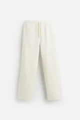 Pantalón de jogging recto color crudo, confeccionado en tejido interlock de algodón con cintura elástica ajustable con cordón, bolsillos frontales y traseros de vivo.