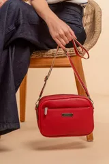 Bandolera roja de cuero sintético con tres cierres principales, cierre delantero y bolsillo trasero. Incluye correa ajustable.