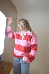 Sweater a rayas rojas y rosas, con cuello tipo polo y mangas largas.