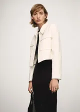Chaqueta corta color crema con rayas verticales finas, cuello camisero, cierre frontal con botones ocultos, manga larga y dos bolsillos de parche en la parte delantera.