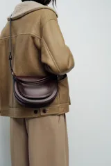 Bolso de hombro ovalado negro con asa de doble tira redonda con detalles metalizados dorados. Cierre imantado y asa de bandolera extraíble con tejido a contraste. Bolso interior con cierre mediante cremallera metálica.